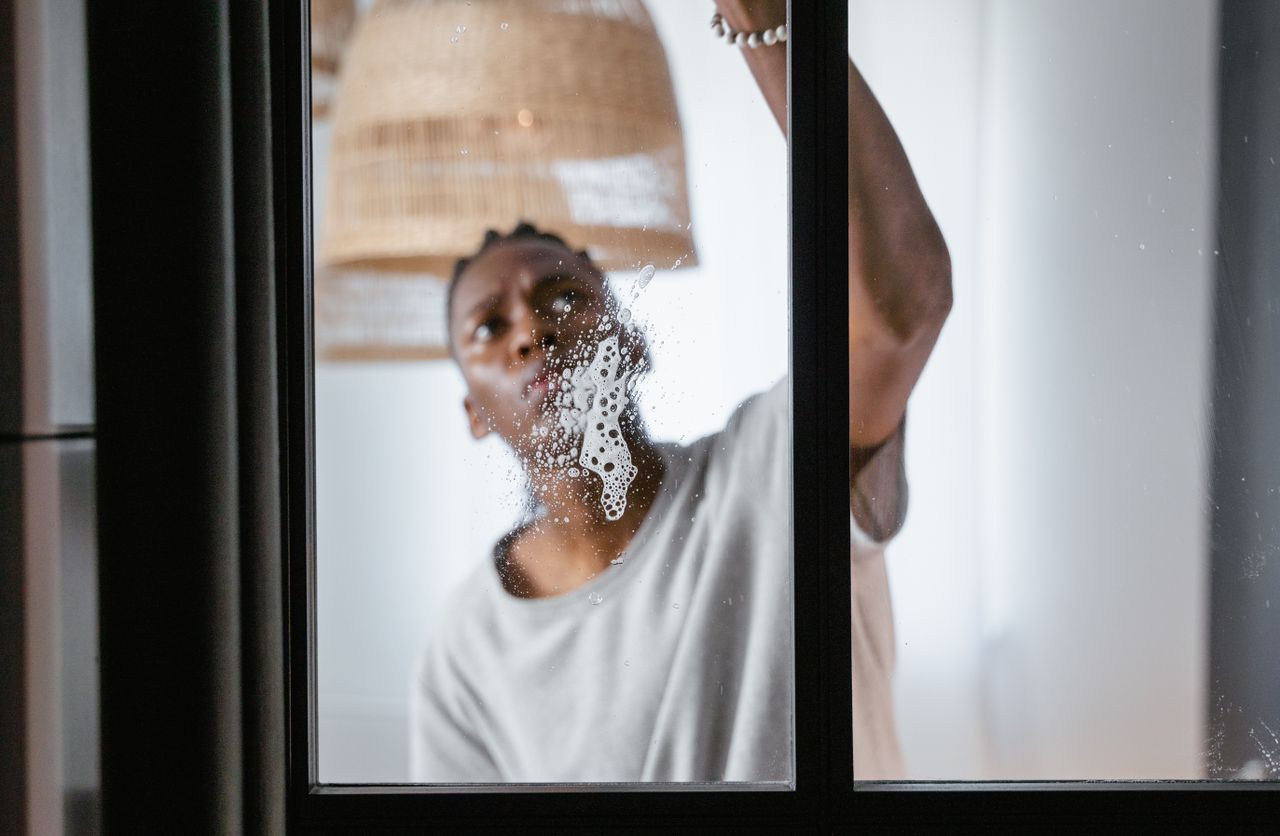An adult man is cleaning an indoor glass window, with attention on household chores and keeping things clean.