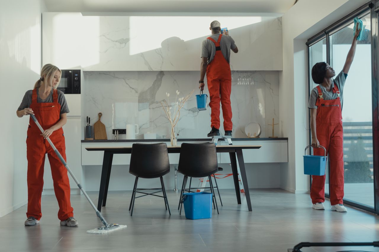 A team of cleaners wearing red uniforms mopping the floor and wiping glass in a modern dining area.
